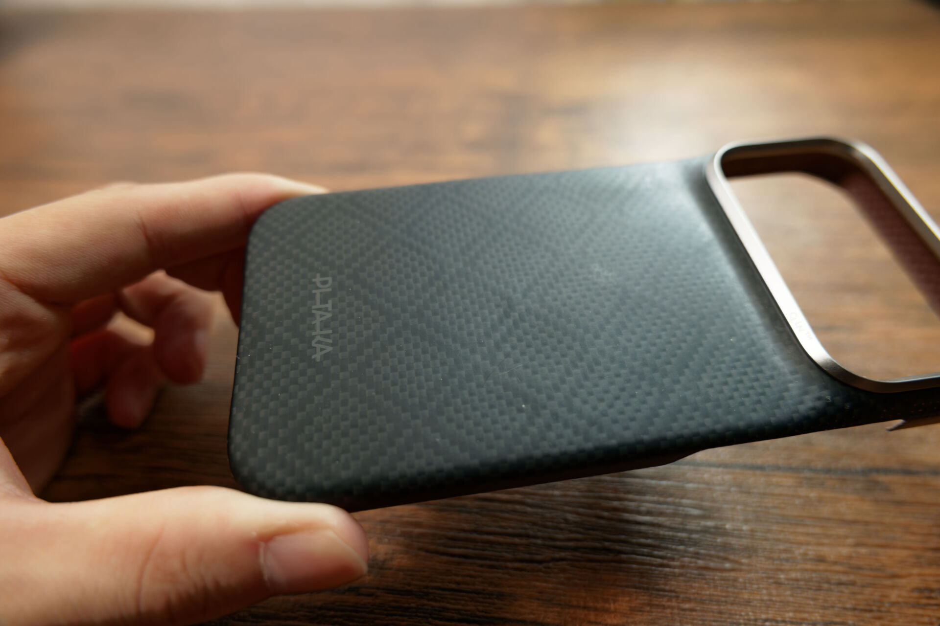 PITAKA Edge Caseを手に持ち、黒いダイヤ柄の背面を見せている